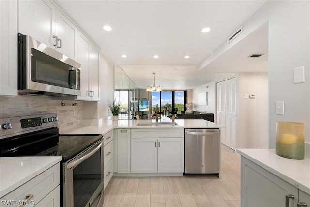 kitchen featuring white cabinetry, stainless steel appliances, a notable chandelier, pendant lighting, and sink