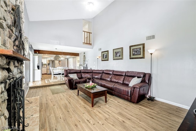 living area featuring a large fireplace, baseboards, visible vents, a towering ceiling, and wood finished floors