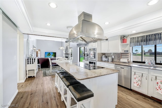 kitchen with a breakfast bar area, a sink, white cabinetry, appliances with stainless steel finishes, and island exhaust hood