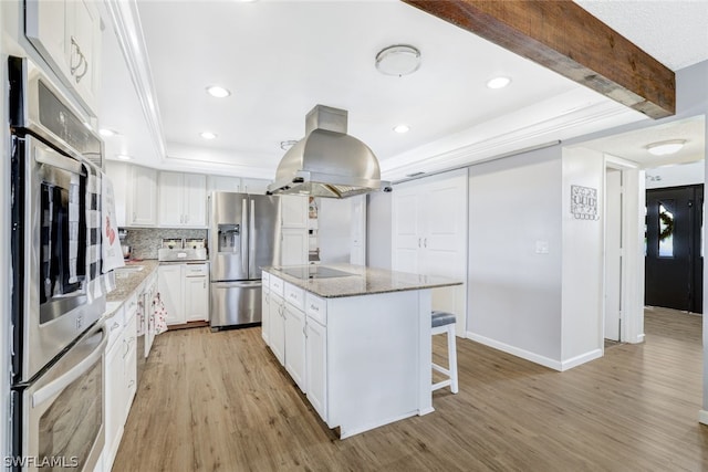 kitchen featuring appliances with stainless steel finishes, white cabinets, island range hood, light stone countertops, and light wood-type flooring