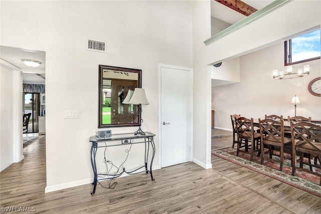 foyer with a high ceiling, wood finished floors, visible vents, and a notable chandelier