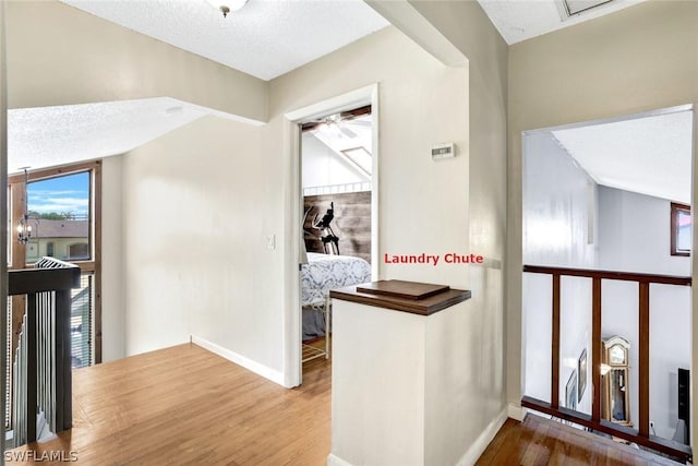 corridor with a textured ceiling, wood finished floors, an upstairs landing, and baseboards