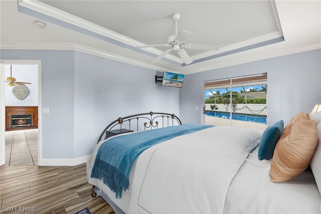 bedroom with wood-type flooring, ornamental molding, access to outside, ceiling fan, and a raised ceiling