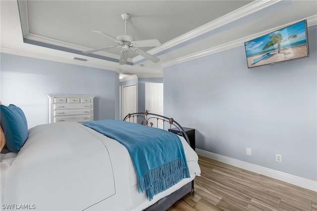 bedroom with wood-type flooring, ornamental molding, ceiling fan, a tray ceiling, and a closet