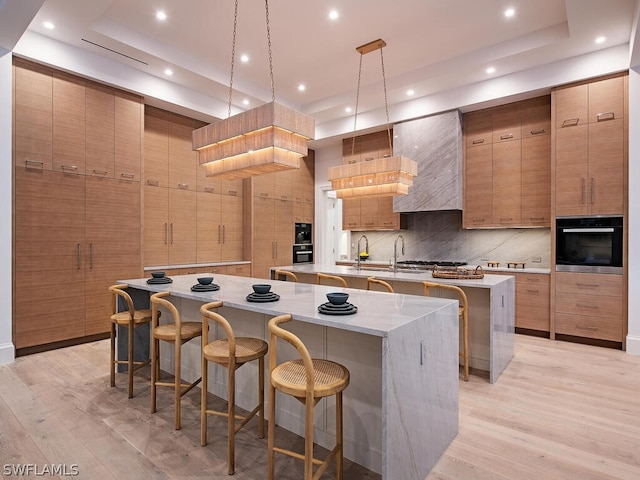 kitchen featuring decorative light fixtures, oven, a spacious island, and light hardwood / wood-style flooring