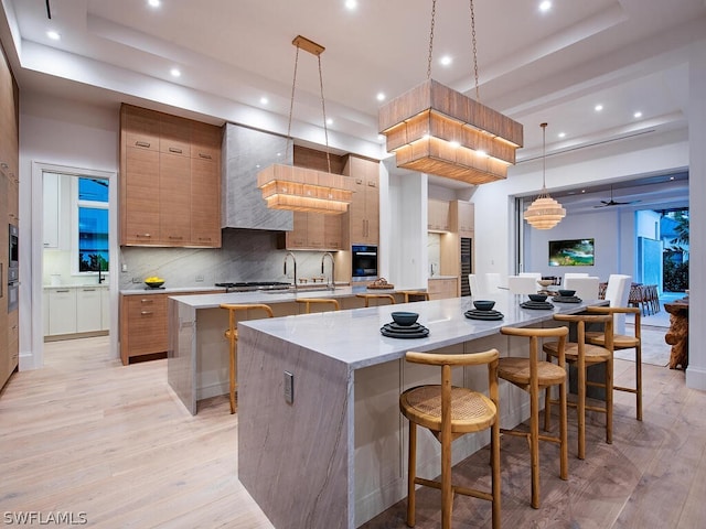 kitchen with pendant lighting, backsplash, light wood-type flooring, and a kitchen island with sink