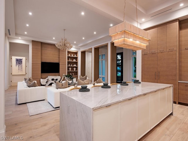 kitchen with light stone countertops, a large island, a notable chandelier, light hardwood / wood-style floors, and decorative light fixtures