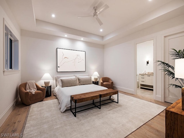 bedroom with a raised ceiling, ensuite bath, ceiling fan, and light hardwood / wood-style flooring