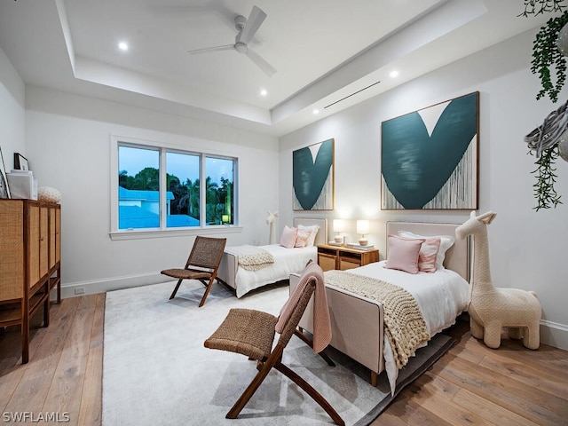 bedroom featuring ceiling fan, light hardwood / wood-style floors, and a tray ceiling