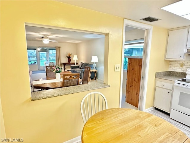 kitchen featuring electric stove, white cabinetry, decorative backsplash, ceiling fan, and light hardwood / wood-style flooring