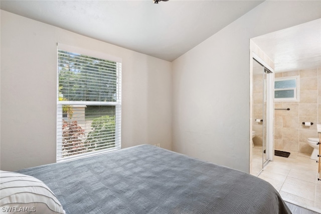 tiled bedroom with tile walls, connected bathroom, and vaulted ceiling