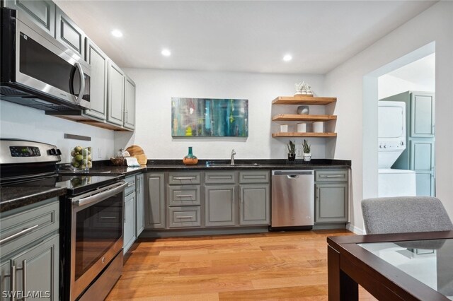 kitchen with light hardwood / wood-style floors, appliances with stainless steel finishes, stacked washer and clothes dryer, and gray cabinetry