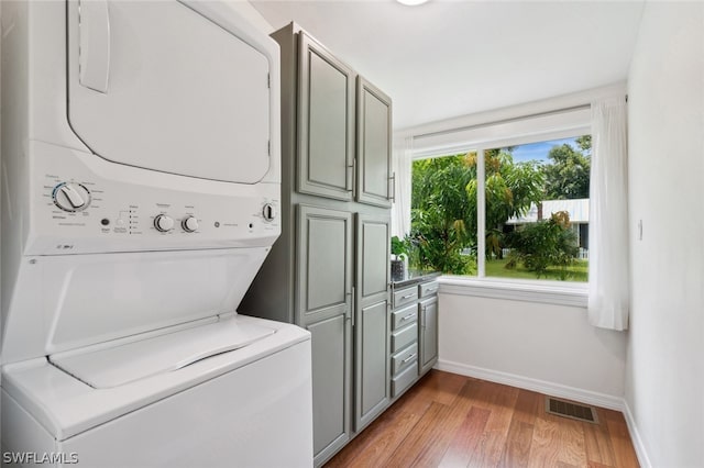 laundry room with cabinets, stacked washer / dryer, and wood-type flooring