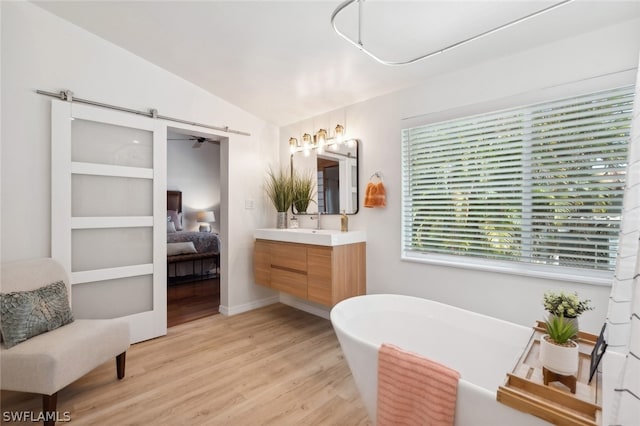 bathroom with vanity, wood-type flooring, vaulted ceiling, and a bathing tub