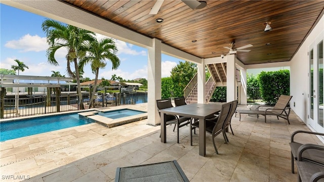 view of patio / terrace with a ceiling fan, a water view, stairs, fence, and a pool with connected hot tub