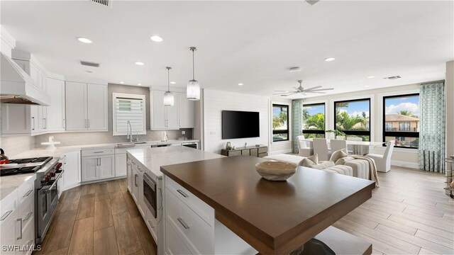 kitchen featuring a center island, range with two ovens, hanging light fixtures, white cabinetry, and wood-type flooring