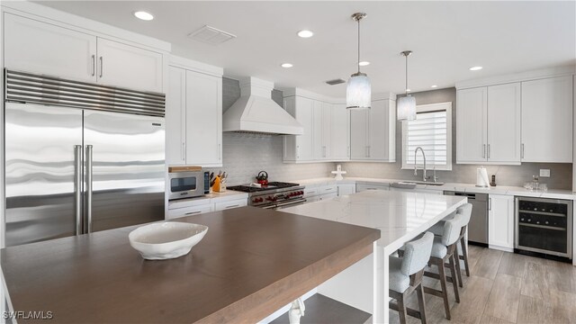 kitchen with custom exhaust hood, white cabinets, decorative light fixtures, wine cooler, and premium appliances