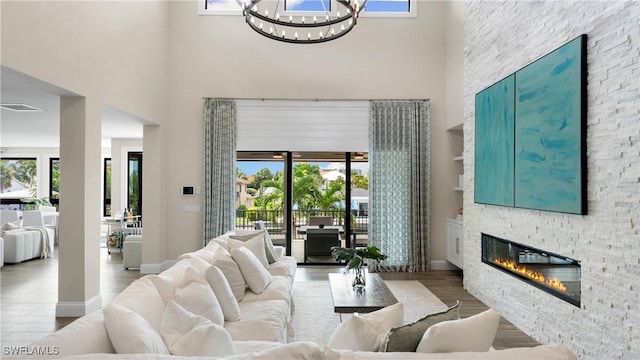 living area with visible vents, a towering ceiling, a stone fireplace, wood finished floors, and a chandelier