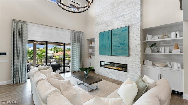 living area featuring a stone fireplace, a high ceiling, wood finished floors, baseboards, and built in features