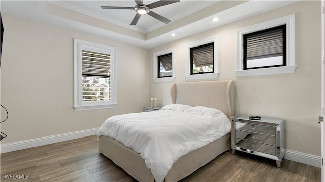 bedroom featuring ceiling fan, ornamental molding, dark wood-type flooring, and a tray ceiling