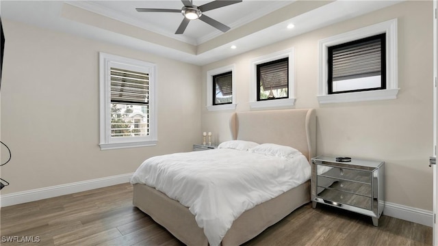 bedroom featuring recessed lighting, wood finished floors, baseboards, a tray ceiling, and crown molding