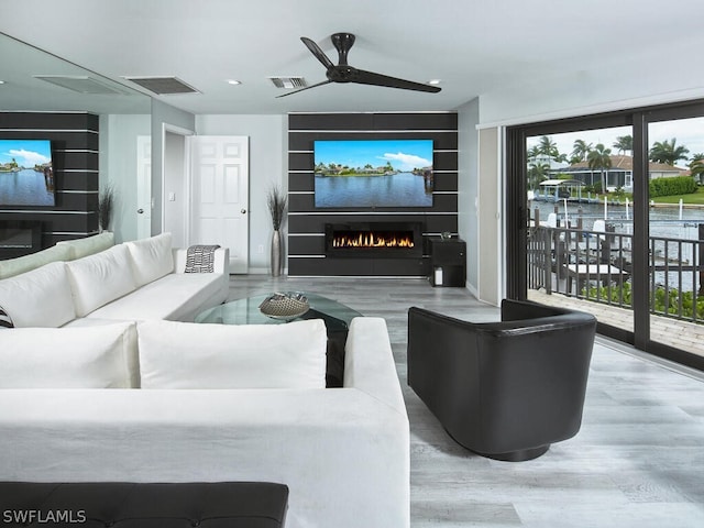 living area featuring visible vents, a ceiling fan, a lit fireplace, and wood finished floors