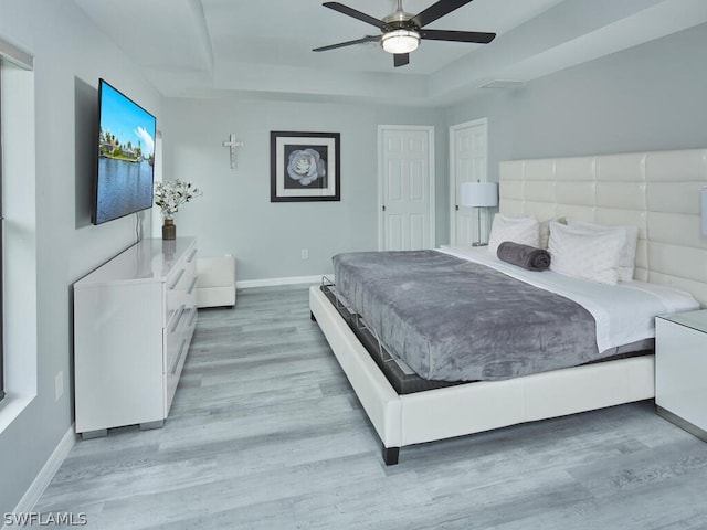 bedroom with a ceiling fan, a raised ceiling, wood finished floors, and baseboards