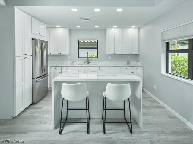 kitchen with stainless steel fridge, a breakfast bar, sink, white cabinets, and a center island