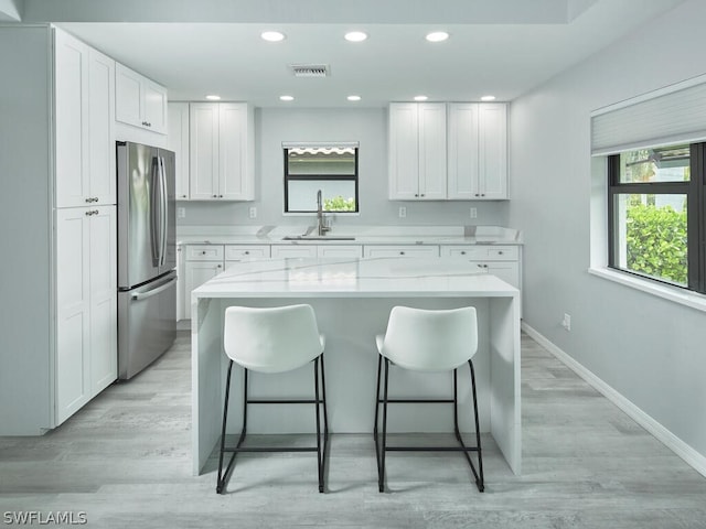 kitchen with a center island, a breakfast bar, freestanding refrigerator, white cabinets, and a sink