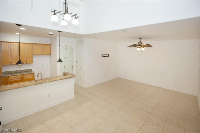 kitchen with light stone countertops, ceiling fan, sink, hanging light fixtures, and a towering ceiling