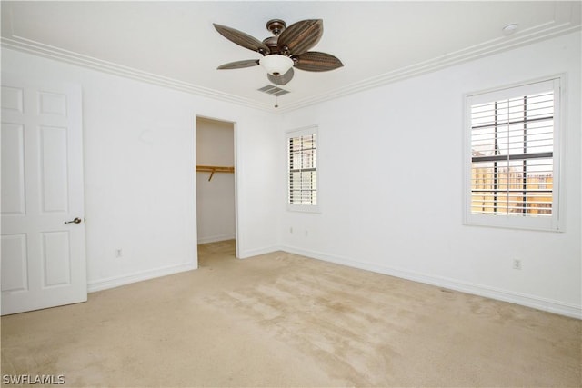 unfurnished bedroom with ceiling fan, a walk in closet, light carpet, a closet, and ornamental molding