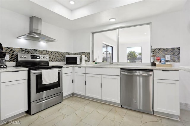 kitchen with a sink, white cabinets, light countertops, appliances with stainless steel finishes, and wall chimney exhaust hood