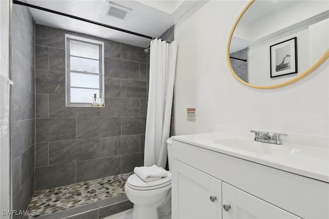 bathroom featuring toilet, visible vents, tiled shower, and vanity