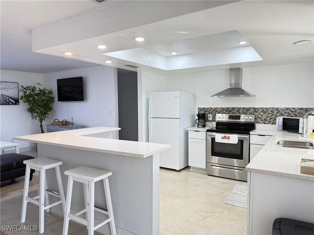 kitchen featuring a kitchen breakfast bar, backsplash, freestanding refrigerator, stainless steel electric range oven, and wall chimney exhaust hood