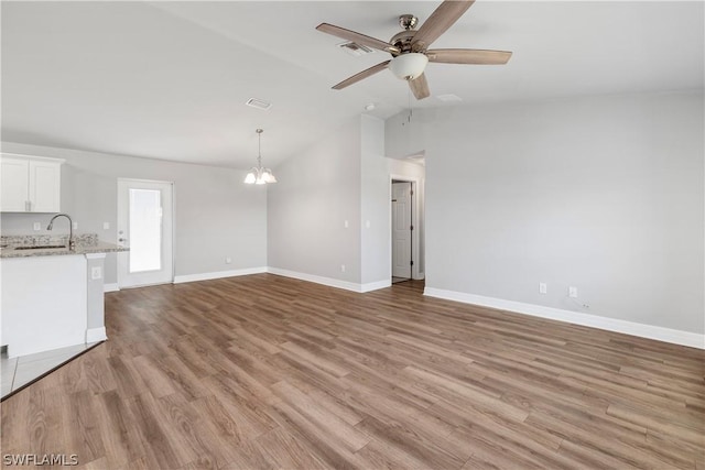 unfurnished living room with ceiling fan with notable chandelier, vaulted ceiling, sink, and light hardwood / wood-style flooring