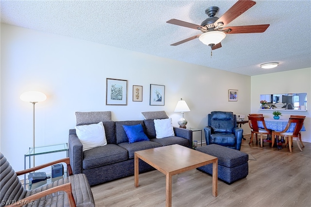 living room featuring ceiling fan, light hardwood / wood-style floors, and a textured ceiling