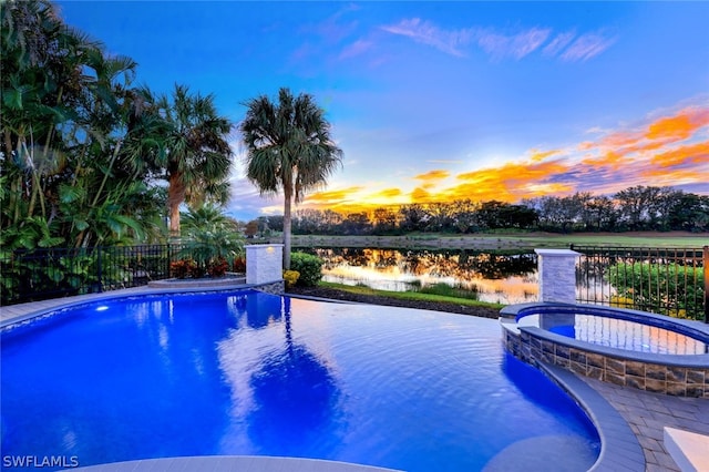 pool at dusk featuring a water view and an in ground hot tub