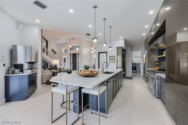 kitchen with sink, a large island with sink, decorative light fixtures, decorative backsplash, and appliances with stainless steel finishes