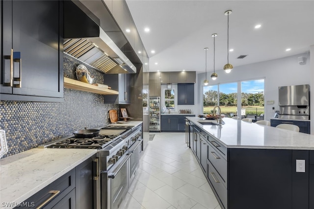 kitchen with light stone countertops, sink, hanging light fixtures, a large island with sink, and appliances with stainless steel finishes