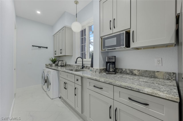 kitchen featuring light stone counters, sink, hanging light fixtures, and independent washer and dryer