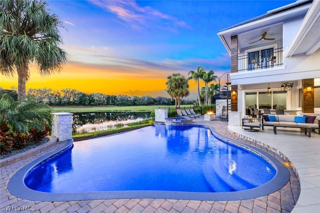 pool at dusk featuring an outdoor living space, a water view, ceiling fan, and a patio area