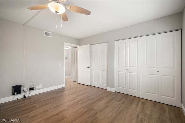 unfurnished bedroom featuring multiple closets, ceiling fan, and hardwood / wood-style flooring