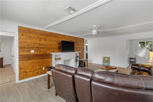 living room featuring ornamental molding, light wood-type flooring, wood walls, and ceiling fan