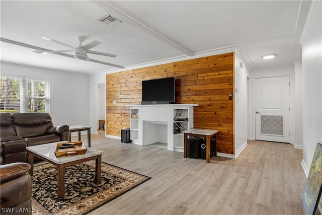 living room featuring light hardwood / wood-style floors, a fireplace, wooden walls, ornamental molding, and ceiling fan