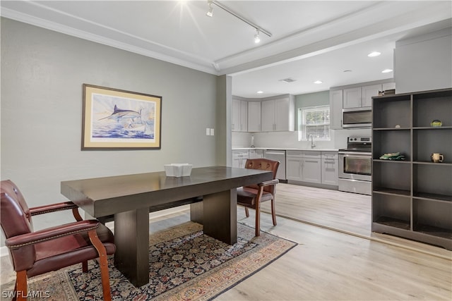 dining area with light wood-type flooring, rail lighting, ornamental molding, and sink