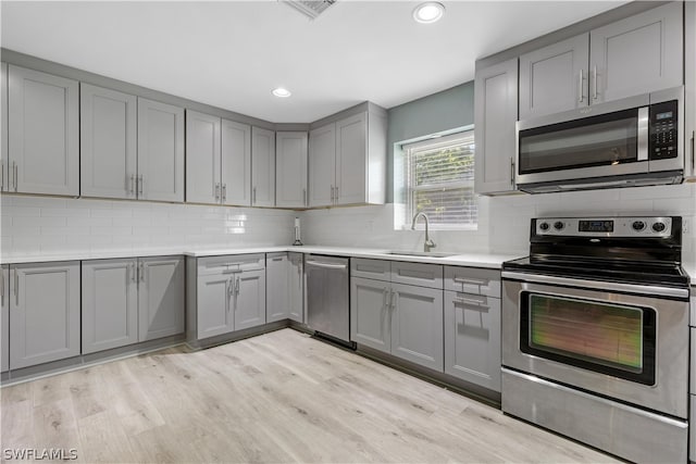 kitchen with tasteful backsplash, gray cabinets, stainless steel appliances, light hardwood / wood-style flooring, and sink