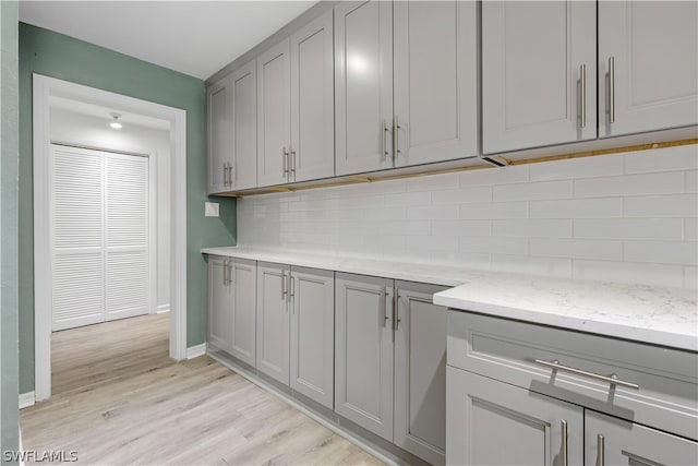 kitchen with gray cabinetry, light stone countertops, light hardwood / wood-style floors, and decorative backsplash