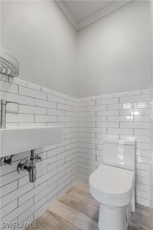 bathroom with hardwood / wood-style flooring, tile walls, crown molding, and toilet