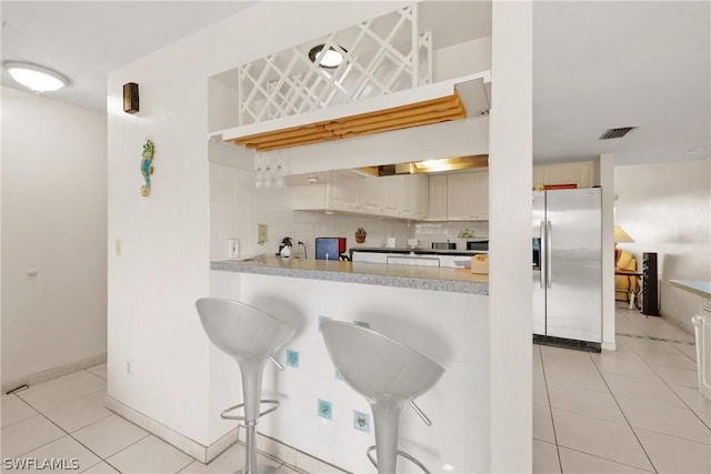 kitchen featuring backsplash, stainless steel fridge, light tile patterned floors, and a breakfast bar area