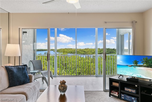 living room featuring a textured ceiling, carpet floors, ceiling fan, and a water view